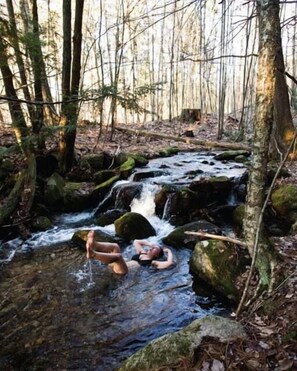 A natural outdoor setting with a small waterfall and a person relaxing in the water.