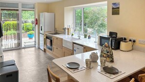 A modern kitchen with a large island, a built-in oven, and a view of the garden through the glass door.