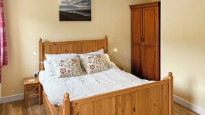 A wooden bed with a headboard, two nightstands, a wooden wardrobe, and a painting on the wall.