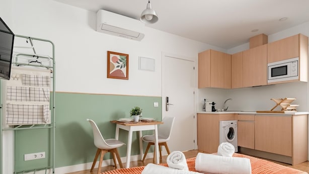 A modern, compact room with a bed, a small dining area, a kitchenette, and a washing machine. - Sol Studio II – In the City Center (Madrid)