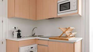 A compact kitchen with a built-in washing machine, a coffee maker, and a microwave. - Sol Studio II – In the City Center (Madrid)