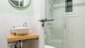A modern bathroom with a round mirror, a white sink, and a glass-enclosed shower. - Sol Studio IV – In the City Center (Madrid)