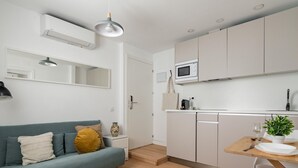 A modern kitchen with white cabinets, a microwave, and a dining area with a table and chairs. - Sol Studio IV – In the City Center (Madrid)