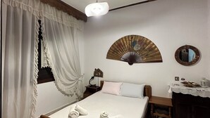 Quarto com cama, mesa de cabeceira, abajur, espelho e leque decorativo na parede.