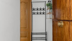 Un armario de madera con un tirador de latón, una estructura metálica negra con ganchos y repisas, y una planta pequeña sobre una estantería.