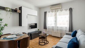 Una sala de estar moderna con comedor, un sofá, un televisor y una ventana con cortinas.