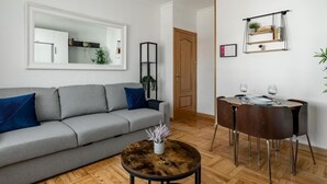 Una sala de estar moderna con un sofá gris, una mesa redonda de centro y un comedor con mesa y sillas de madera.