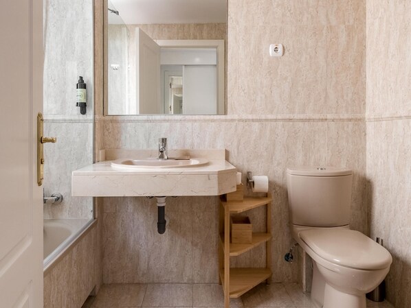 A bathroom with a marble sink, a toilet, and a mirror.
