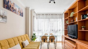 A living room with a sofa, TV, wooden shelving, and a dining area with chairs and a table.