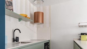 Et moderne køkken med vask, komfur og mikrobølgeovn. Der er en hylde over vasken og en hængende lampe.