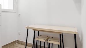Et lille, minimalistisk rum med en hvid væg, et vindue og et simpelt træbord med to hylder.