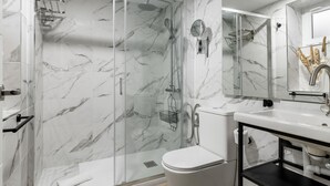 Et moderne badeværelse med en brusekabine med glasdøre, et hvidt toilet og en vask med en sort bordplade.