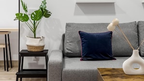 En moderne stue med en grå sofa, en mørkeblå pude, en hvid vase og en plante i en vævet kurv.