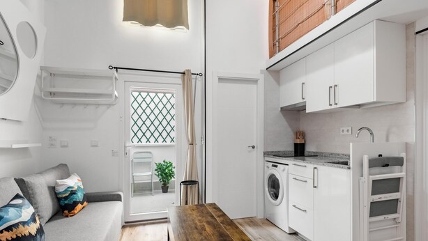 Een compact woongedeelte met een bank, een houten zitting, een wasmachine en een kitchenette.