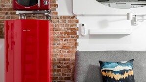 Een keuken met een rode apparatuur, een bakstenen muur en een grijze bank met een decoratief kussen.
