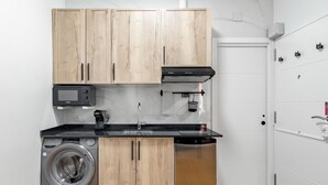 Een compacte keuken met houten kastjes, een wasmachine, een vaatwasser, een magnetron en een rvs afzuigkap.