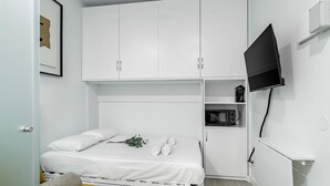Un dormitorio pequeño con cama, un sofá, televisión y microondas.