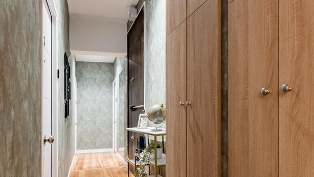 Un pasillo estrecho con suelo de madera, una puerta de cristal y una estantería con objetos decorativos.