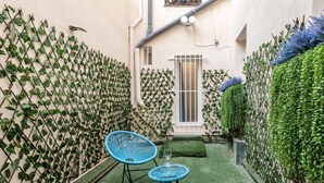 Un pequeño patio al aire libre con césped artificial, dos sillas azules y una mesita.