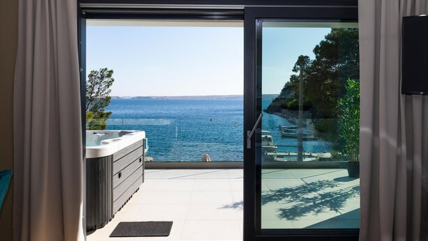 A room with a sliding glass door leading to a balcony with a hot tub and a view of the sea. - Lovely home in Baric Draga (Baric Draga)