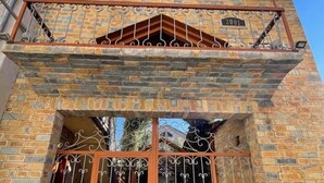 Un edificio de dos pisos con fachada de piedra, un balcón con barandilla metálica y un gran portón de metal con adornos.