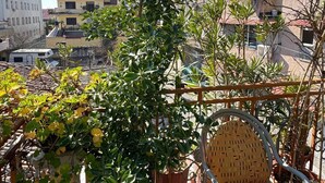 Un balcón con plantas en macetas, una silla de mimbre y vistas de los edificios circundantes.