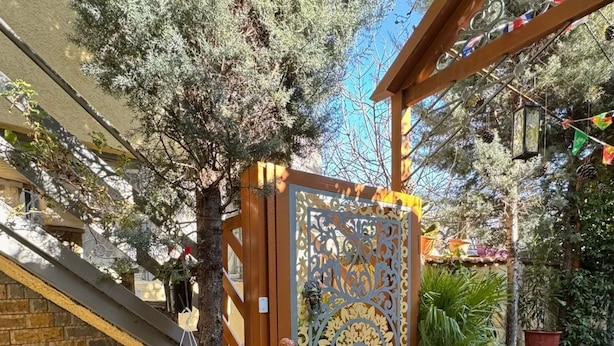 Una entrada protegida con una puerta metálica decorativa, plantas en macetas y un felpudo.