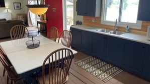 A kitchen with a dining area, wooden chairs, a white table, and a red door. - Ostrander's 3 Bedroom Cottage on Rice Lake (Harwood)