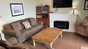 A living room with a sofa, a coffee table, a fireplace, a television, and a cabinet. - Ostrander's 3 Bedroom Cottage on Rice Lake (Harwood)