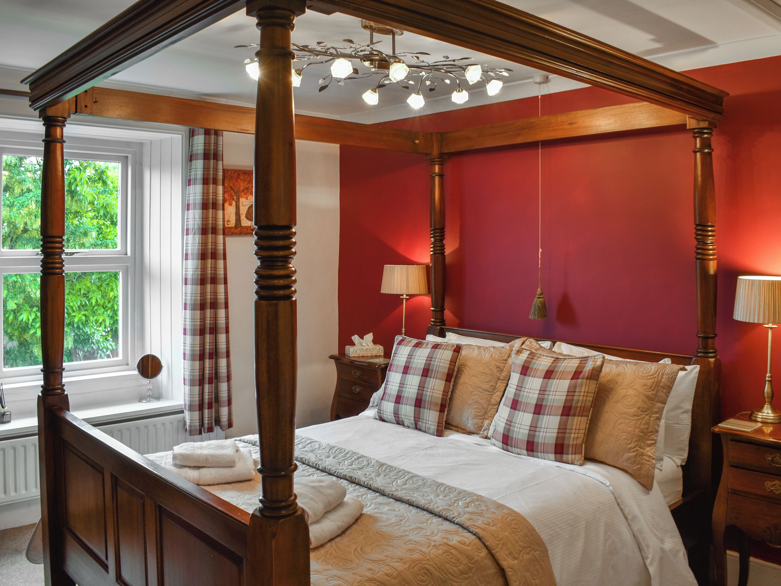 A four-poster bed with a canopy, a bedside table, a lamp, and a window with curtains.