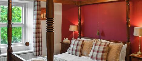 A four-poster bed with a canopy, a bedside table, a lamp, and a window with curtains.