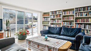 A living room with a blue sofa, a coffee table with a floral tablecloth, and a bookshelf filled with books.