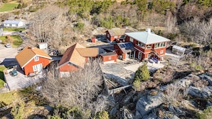A large, multi-story house with a red exterior and a green roof, surrounded by trees and rocky terrain.