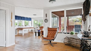 A spacious room with wooden flooring, a large window, a bed, a chair, and a sewing machine.