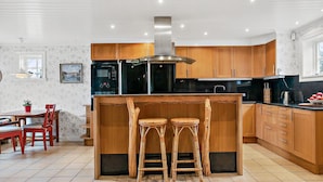 A modern kitchen with wooden cabinets, a central island with stools, and a dining area with a table and chairs.