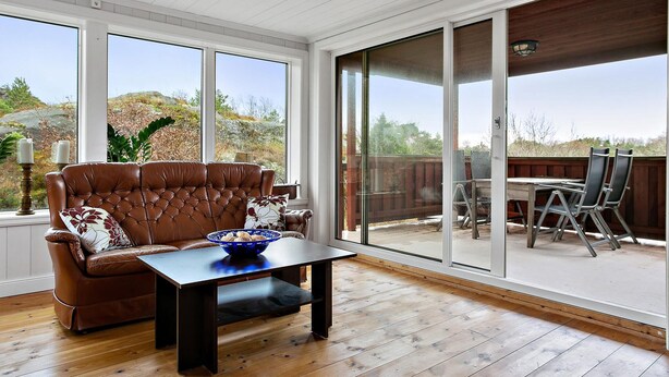 A room with a leather sofa, a wooden coffee table, and a large sliding glass door leading to an outdoor patio with a table and chairs.