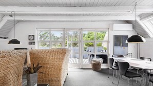 A modern, well-lit room with a large window, a dining area with chairs, and a wicker partition. - 3 bedroom stunning home in Vestervig (Vestervig)