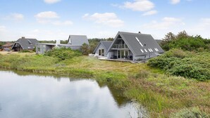 A modern house with a sloped roof, large windows, and a view of a body of water. - 3 bedroom stunning home in Vestervig (Vestervig)