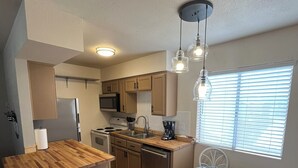 A compact kitchen with wooden countertops, a stainless steel sink, and a dining area with a glass table and white chairs. - Cute Condo in Downtown Area! (Lake Havasu City)