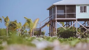 A wooden structure with a metal roof, elevated on stilts, surrounded by greenery and palm trees. - Barbuda Cottages 2 bed ( Green ) Beachfront Villa
 (Codrington)