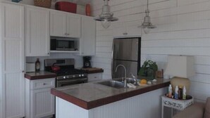 A kitchen with white cabinetry, a central island, a microwave, a stove, and a sink. There are pendant lights above the island and a ceiling fan. - Barbuda Cottages 2 bed ( Green ) Beachfront Villa
 (Codrington)