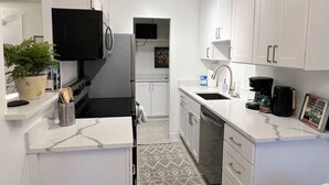 A compact kitchen with white cabinetry, a built-in oven, a microwave, a coffee maker, and a small rug.
