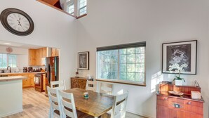 Une cuisine spacieuse avec des meubles de rangement en bois, une table à manger avec des chaises, une grande fenêtre et une horloge au mur.