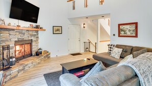Un salon doté d’une cheminée en pierre, d’un téléviseur à écran plat, d’un canapé et d’un escalier menant à l’étage supérieur.