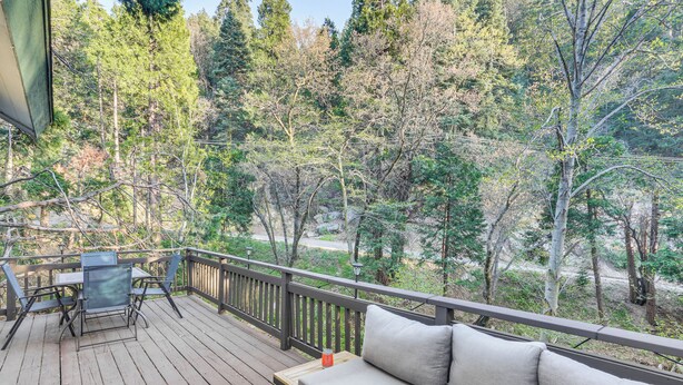 Une terrasse en bois avec un canapé et des fauteuils, donnant sur une zone boisée.
