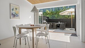 A modern dining area with a round table and white chairs, a pendant light, and a view of an outdoor patio with a grill and umbrellas. - 3 bedroom lovely home in Gilleleje (Gilleleje)