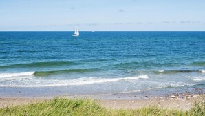 A beach with a sailboat in the distance and a rocky shoreline. - 3 bedroom lovely home in Gilleleje (Gilleleje)