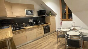A modern kitchen with wooden cabinets, a black countertop, and a dining area with a round table and chairs. - 19A - The Seventh Heaven, cocoon lover (Tulle)