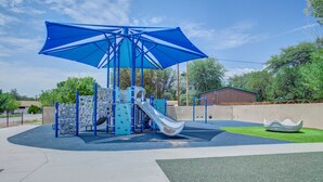Un parque infantil con un tobogán, estructuras para escalar y una sombrilla azul.