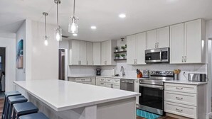 A modern kitchen with white cabinets, stainless steel appliances, and a central island with bar stools. - Pickleball + Heated Pool | Near Anna Maria (Sarasota)